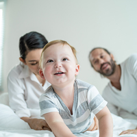 Bébé joyeux dans le lit avec ses parents derrière lui